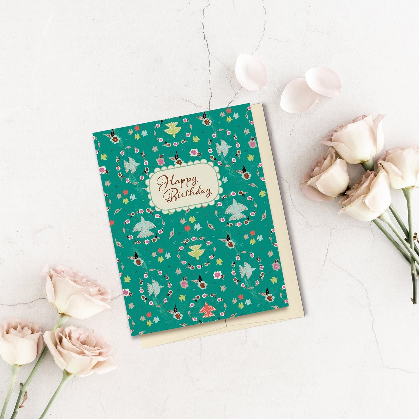 Birds & Floral Wreaths Happy Birthday Card is perfect for that special lady's birthday. Created with a vibrant teal background, this card features a layered look with texture, multi-colored flowers and birds, details reminiscent of Grandma's lace and scripted text which reads, "Happy Birthday." The pattern continues onto the back of the card. Displayed on a concrete background and surrounded by pink roses.