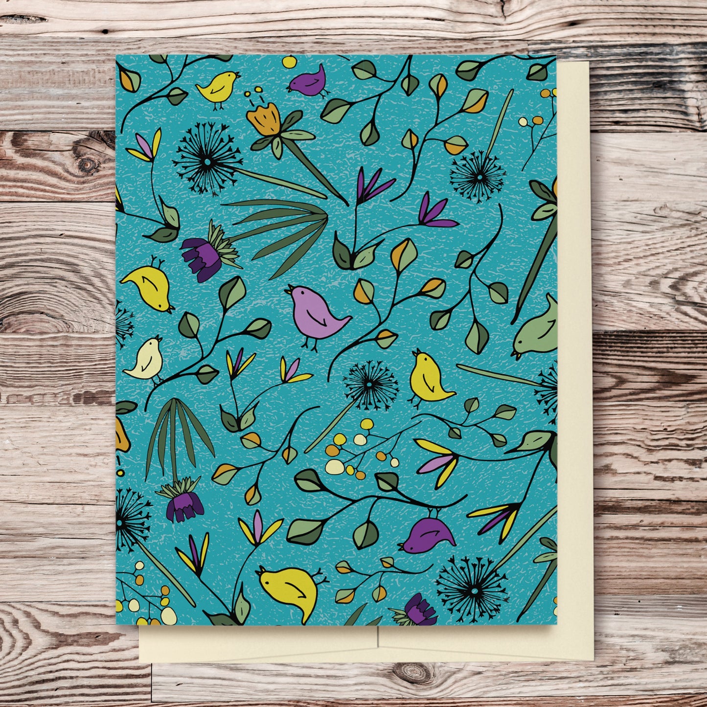 Flowers & Birds Turquoise Blank Card features a hand drawn pattern with birds and flowers in shades of purple, yellow and green on a turquoise background. The pattern extends over the back of the card too. Card displayed on wooden background.