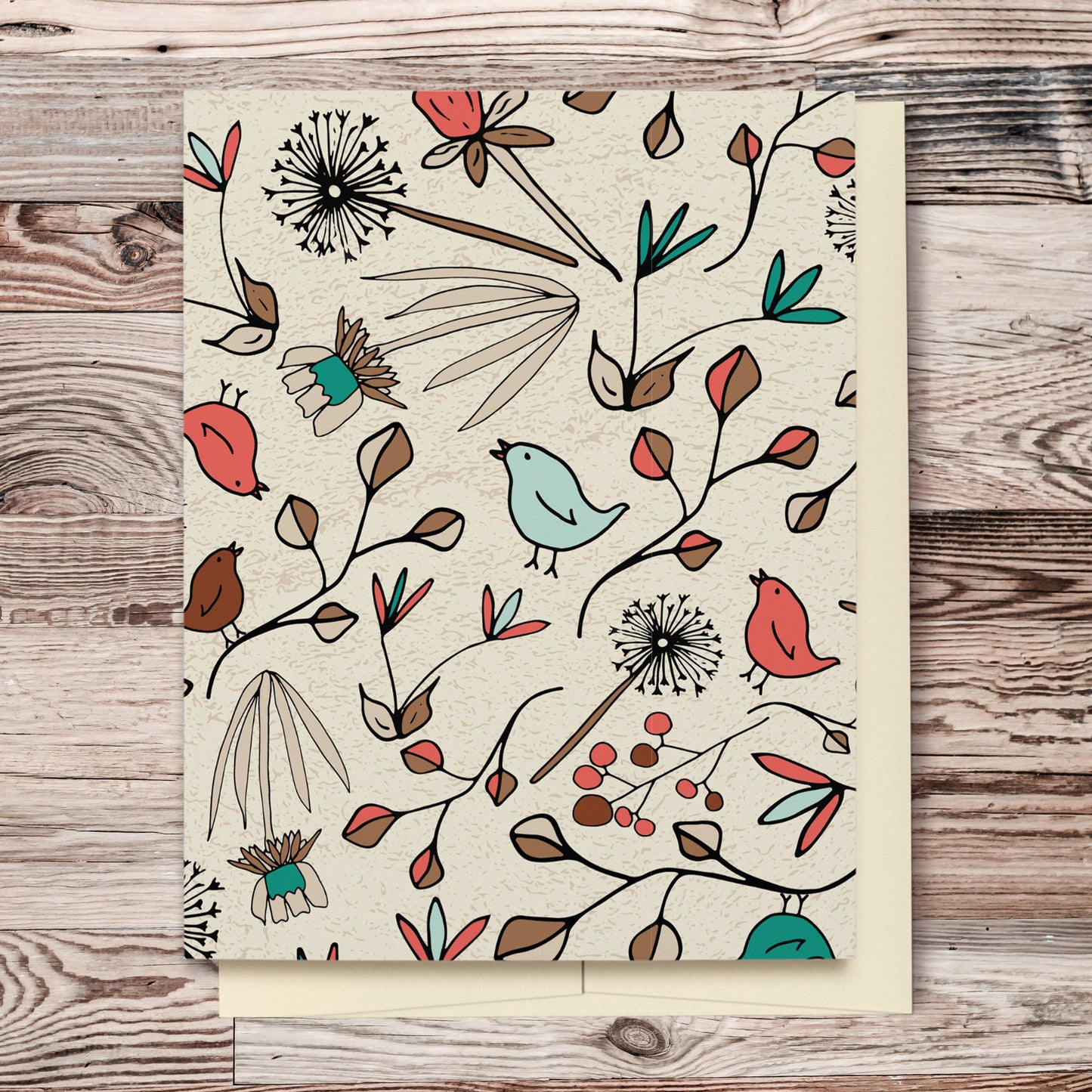 Flowers & Birds Cream Blank Card features a pattern with birds and flowers in shades of green, orange and brown on a cream background. The pattern extends over the back of the card too. Displayed on a wooden background.