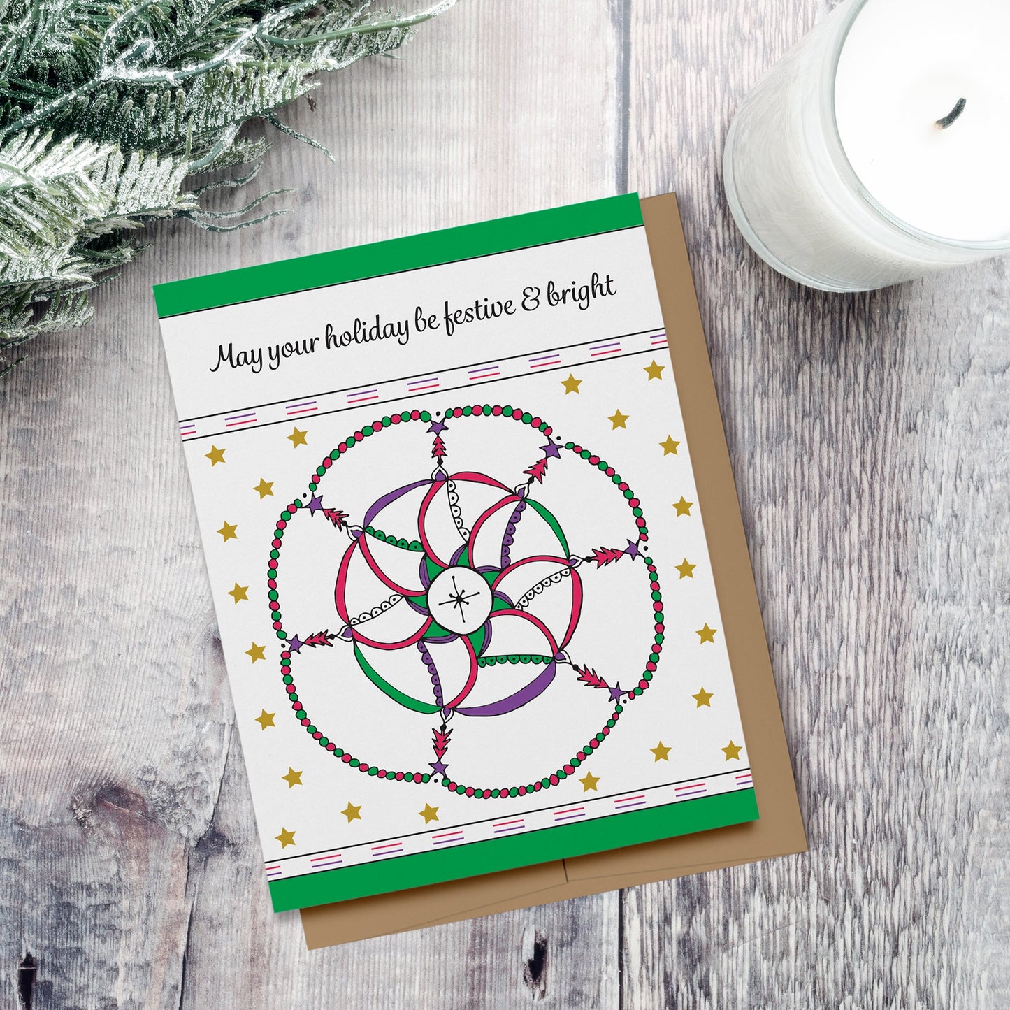Colorful holiday card with a hand drawn mandala featuring trees and stars on a star-filled background with text which reads, "May your holiday be festive & bright." Displayed on a wood background with a candle and evergreen branch.