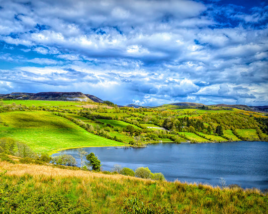 Ireland Photography featuring a lake with mountains in the background against a blue sky with moody clouds.